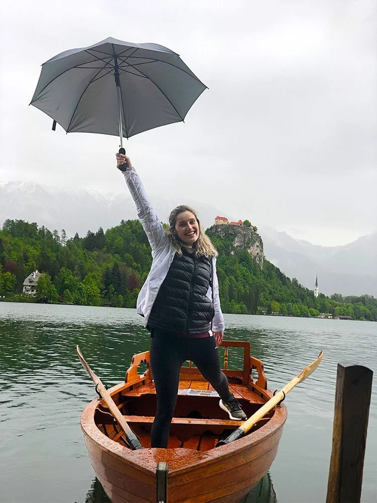 Sara dentro de barco a remos com um guarda-chuva na mão, no Lago Bled