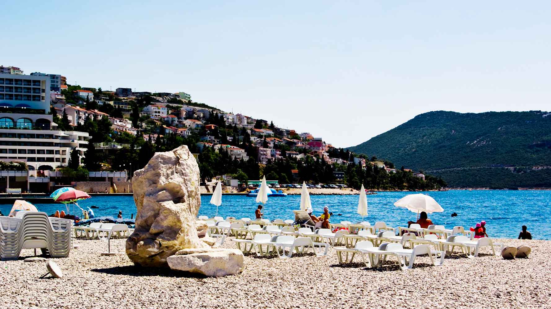 Vista da praia de Neum para a encosta com edifícios de alojamento e restauração.