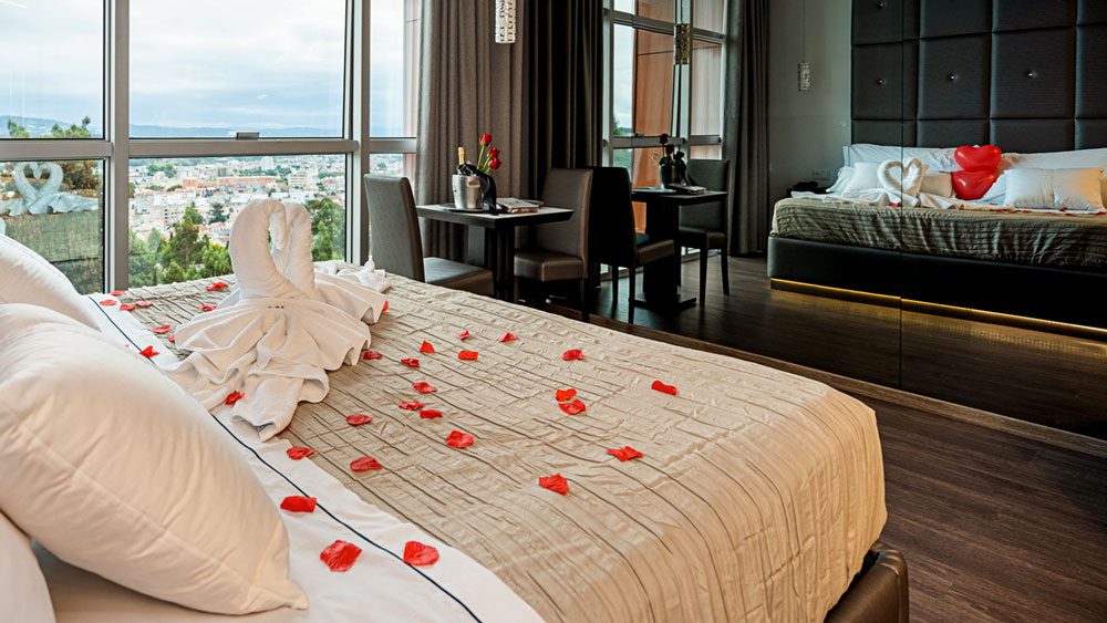 Suite Lux com decoração romântica de cisnes e pétalas de rosa sobre a cama, no Motel Alto de Valongo