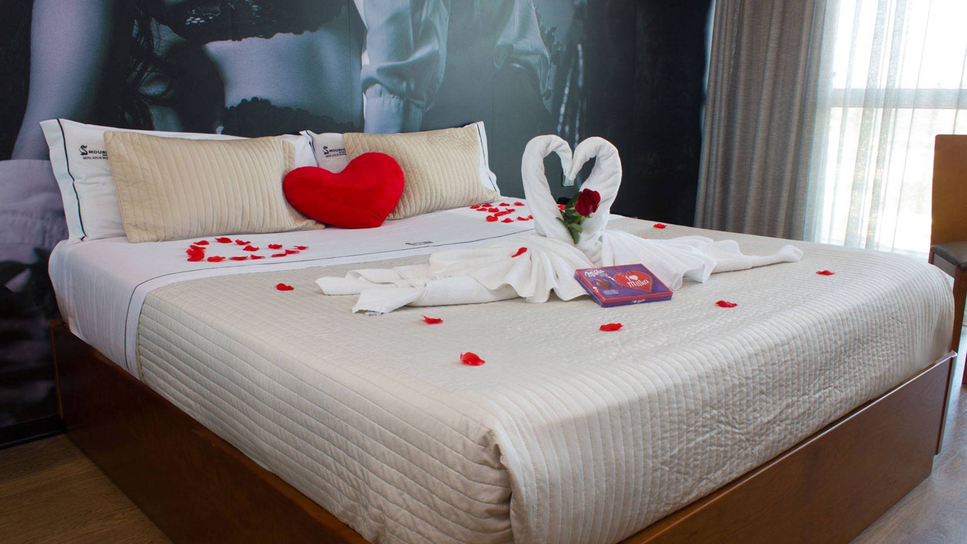 Cama da suite Premium do Motel Alto de Valongo com cisnes, pétalas de rosa e chocolates