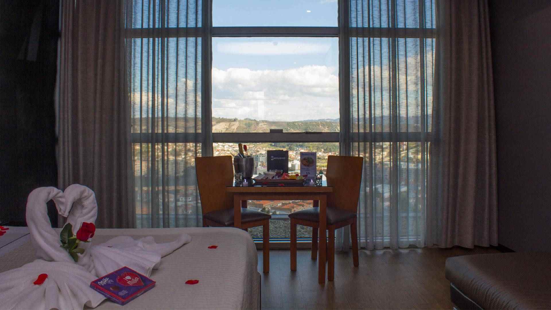Suite Premium com decoração de cisnes, rosas e chocolates em cima da cama e uma garrafa de champanhe sobre a mesa, no Motel Alto de Valongo