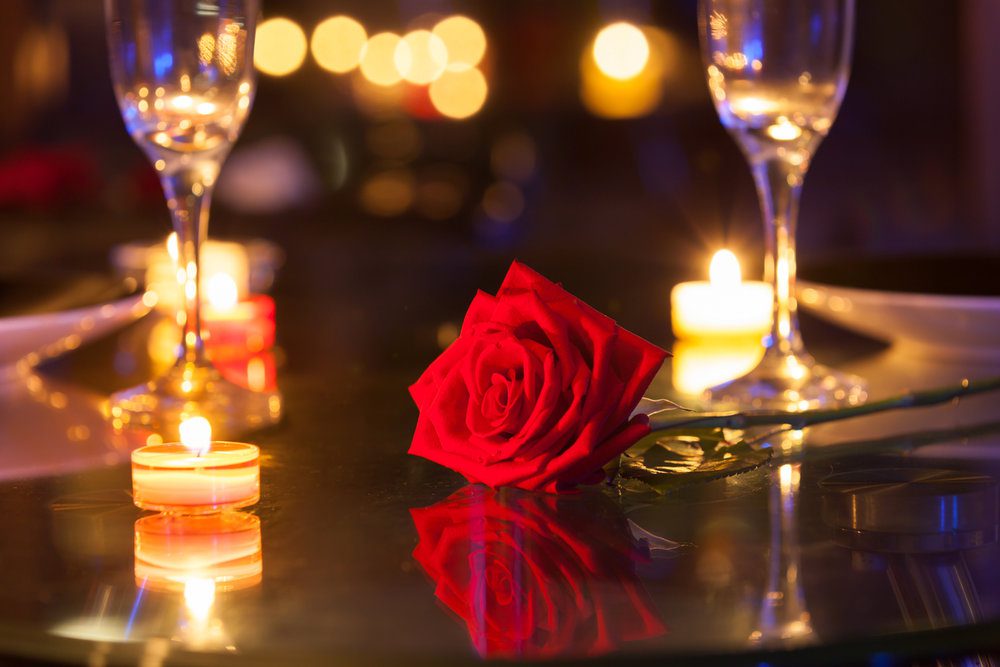 Imagem de pormenor de rosa vermelha, flutes de champanhe e velas sobre a mesa