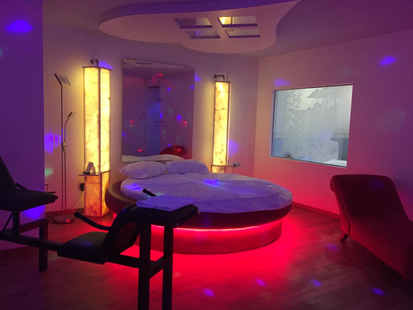 Quarto do Motel D'lirius Azuis com cama redonda, cadeira tântrica, espelhos no tecto e iluminação em tons vermelhos