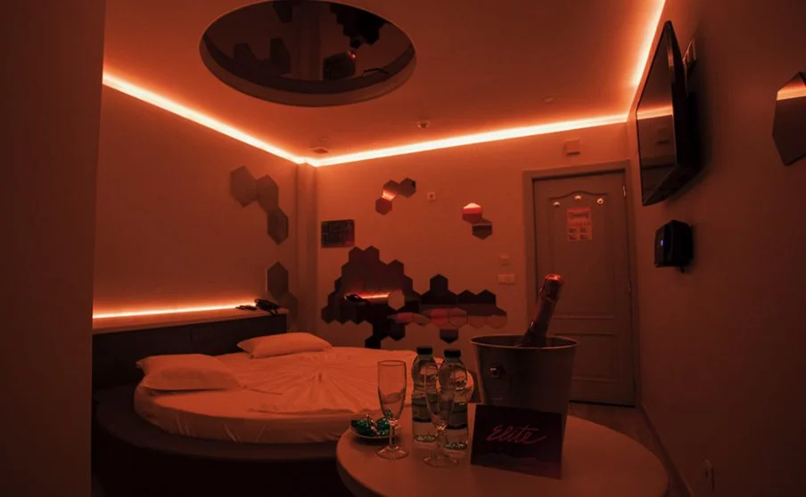 Suite com cama redonda, espelhos, luzes vermelhas e à frente uma garrafa de champanhe, duas flutes e garrafas de água no Elite Motel.