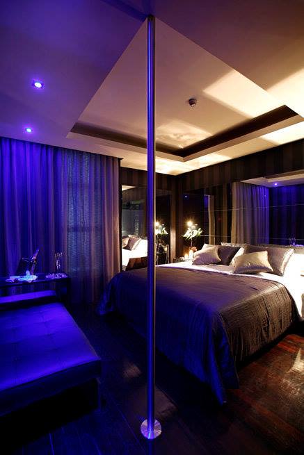 Zona de dormir à média-luz com luzes roxas e varão, na suite Nova Iorque, no Motel Flamingo