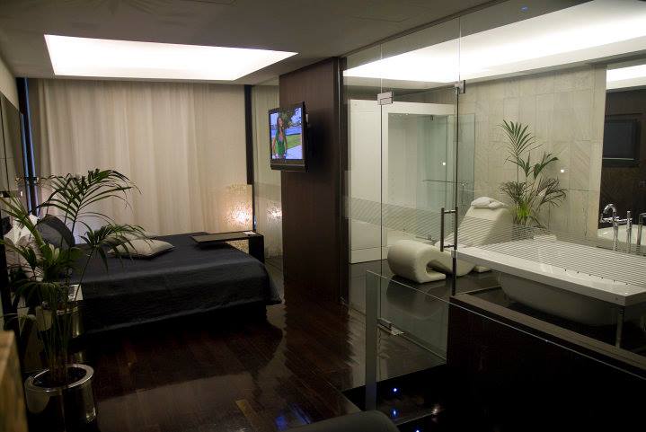 Vista geral da Suite Flamingo, com a zona de jacuzzi e sofá erótico e zona de dormir, com tv e mesa de apoio.