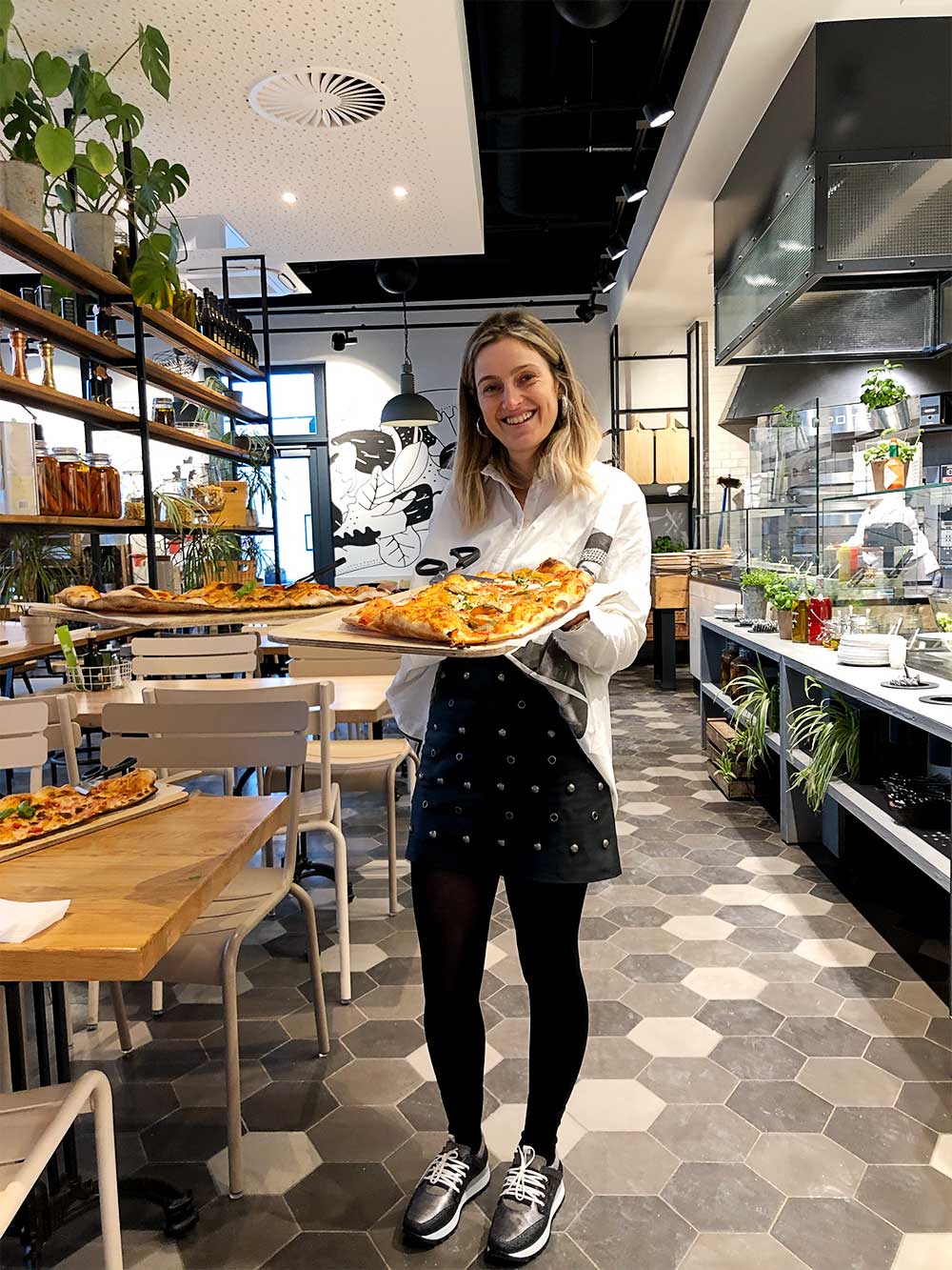 Sara com uma travessa de pizza na mão em Berlim, na pizzaria designer outlet.