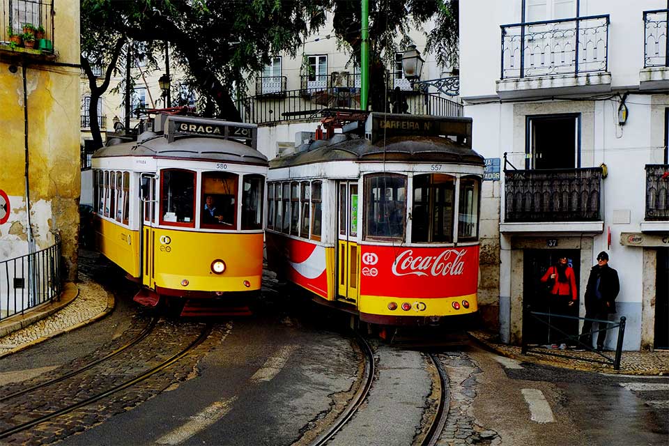 Dois elétricos a descer uma rua estreita no centro histórico da cidade de Lisboa.