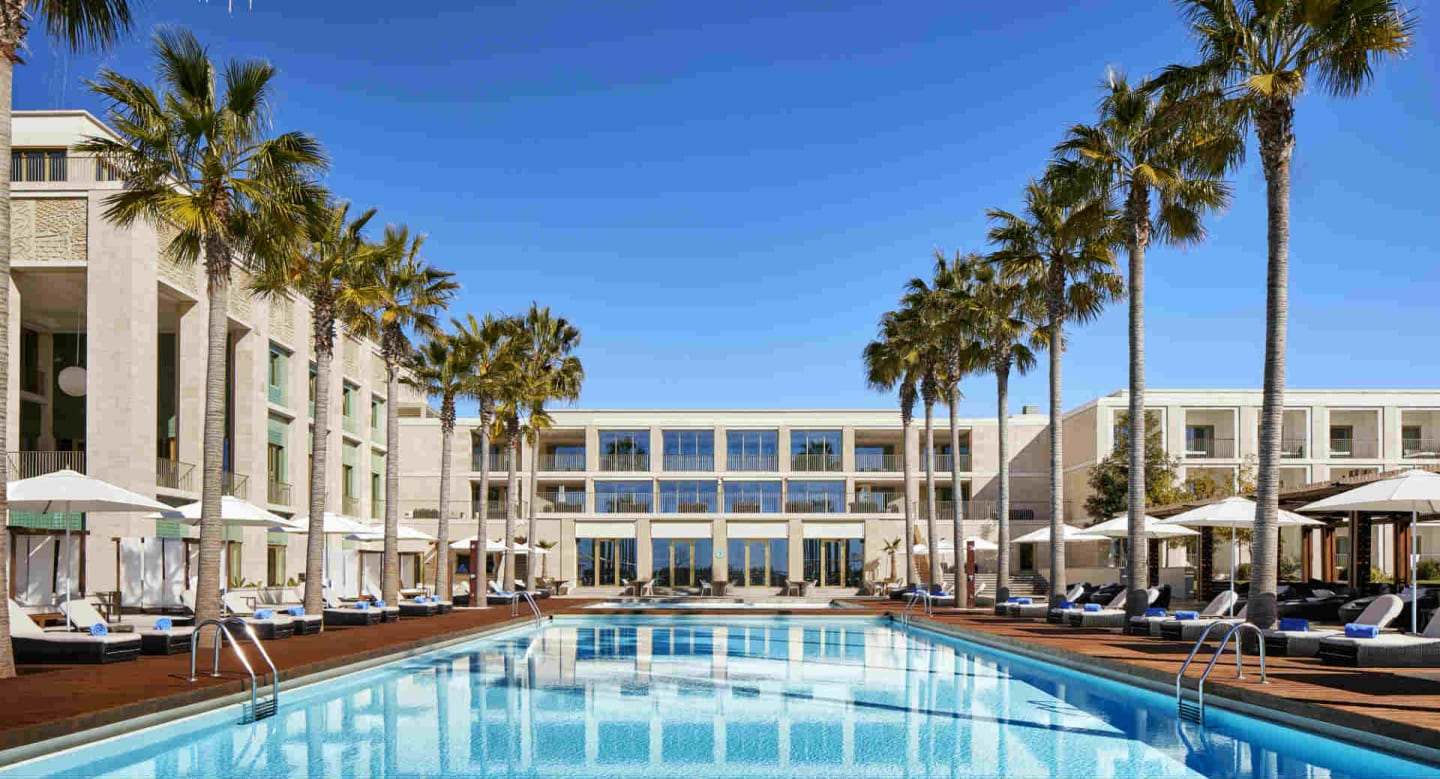 Exterior do Anantara Vilamoura Algarve Resort com piscina, palmeiras e espreguiçadeiras por baixo dos guarda-sóis