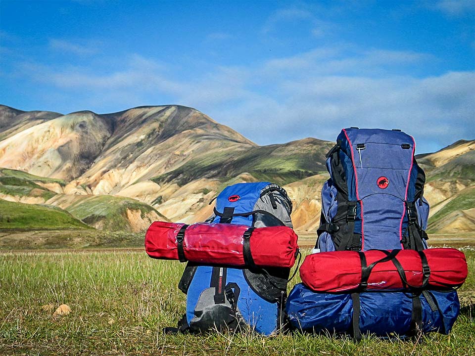 Duas mochilas com material de campismo pousadas no chão junto a montanhas no Brasil.