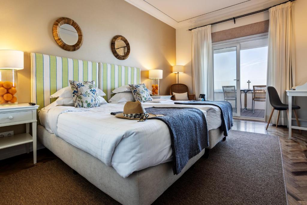 Quarto de hotel com cama twin, secretária e varanda com vista para o mar na Pousada de Sagres.