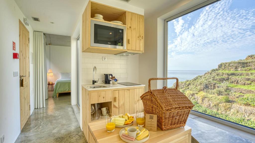 Cozinha com cesta de piquenique em cima da mesa e janela com vista para o mar e para a montanha, no Socalco Nature Calheta, na Calheta