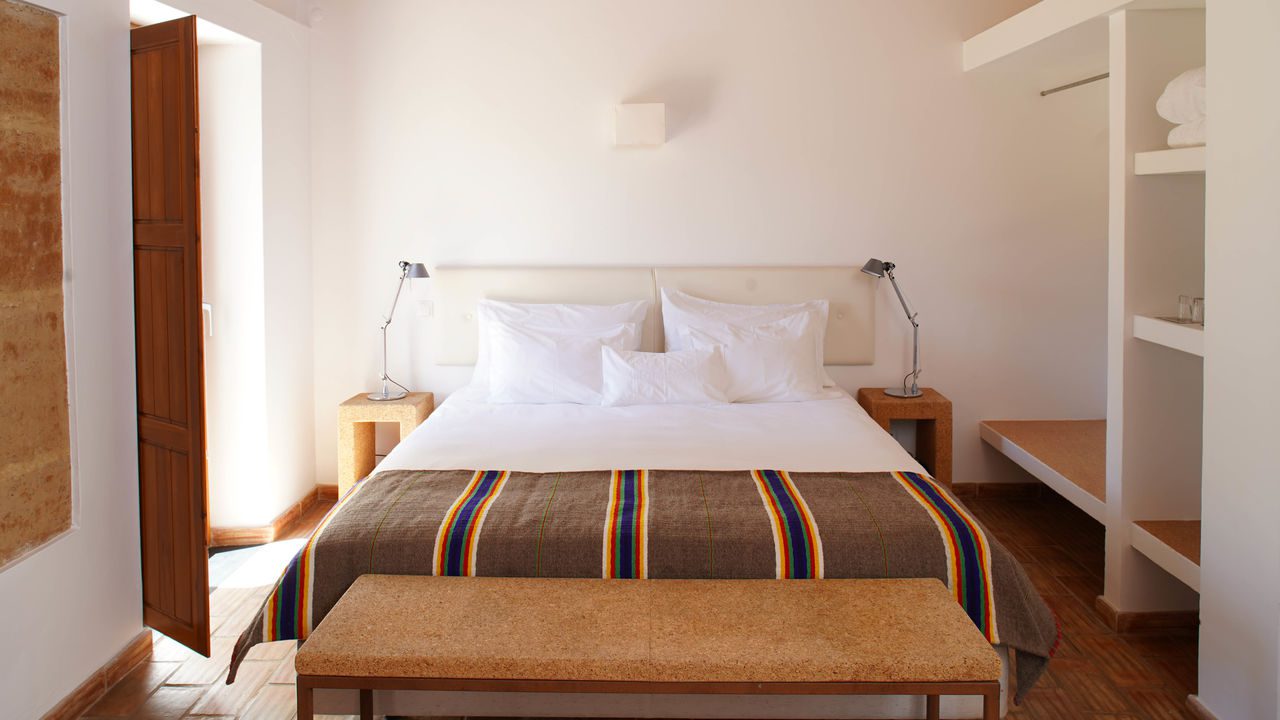 Quarto minimalista com cama de casal, janela e decoração com detalhes em cortiça, no Monte da Vilarinha